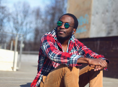 Outdoor fashion portrait of stylish young african man listens to music and enjoys freedom in the...