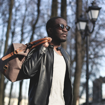Fashion portrait of handsome african man in black leather jacket with bag outdoorsの写真素材