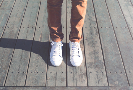 Fashion hipster cool man with white sneakers close-up stands on wooden floorの写真素材