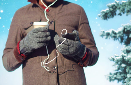 Man listens to music on a smartphone holds coffee cup in hand on a christmas tree background