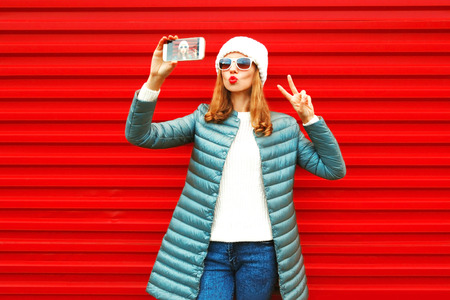 Fashion pretty woman takes a picture self portrait on a smartphone on red backgroundの写真素材