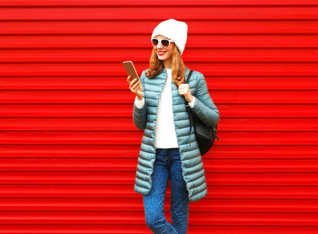 Fashion smiling woman is using smartphone on red backgroundの写真素材