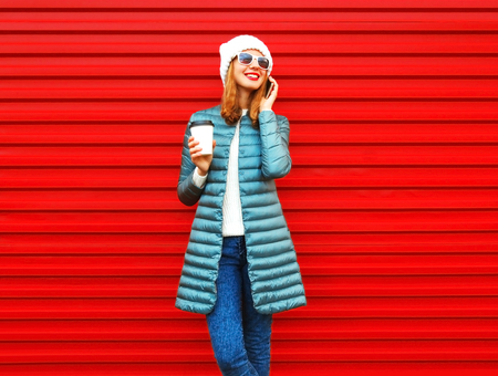 Fashion smiling woman talks on a smartphone holds coffee cup on red background 
の写真素材