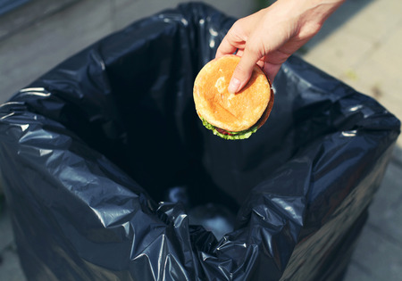 Fast food and unhealthy eating concept - hand throwing a burger in the trash on streetの写真素材