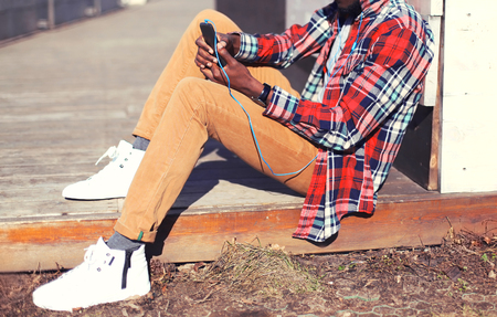 Fashion man listens to music using the smartphone sitting in the city close-upの写真素材