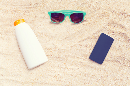 sunglasses, frameless smartphone, sunscreen bottle on white sand beach backgroundの写真素材