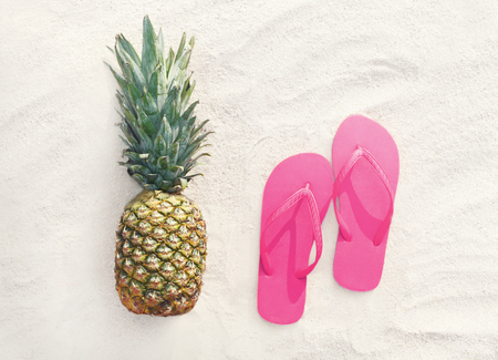 Pineapple fruit and pink flip flops on a beach white sand background, top viewの写真素材