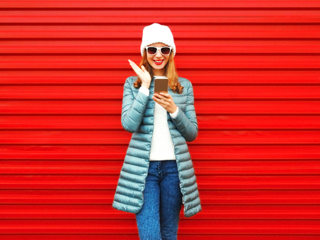 Happy emotional woman is laughing with a smartphone on a red backgroundの写真素材
