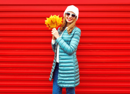 Fashion autumn smiling woman with yellow maple leaves in hands on a red backgroundの写真素材
