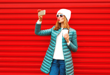 Fashion pretty woman takes a picture self portrait on a smartphone on red backgroundの写真素材