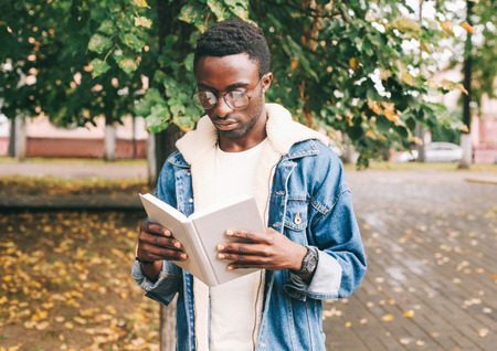 Fashion african man reading book in autumn city parkの写真素材