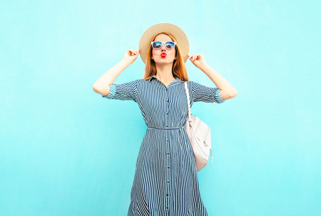 Fashion woman in a striped dress and summer round straw hat on blue backgroundの写真素材