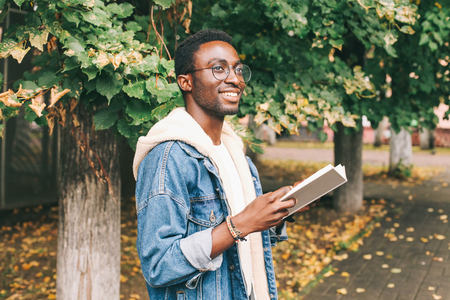 Happy smiling african man holds book in autumn dayの写真素材