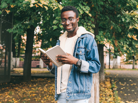 Portrait happy smiling african man reading book in autumn city parkの写真素材