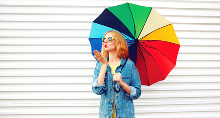 Fashion portrait woman with colorful umbrella sends an air kiss on white background in cityの写真素材