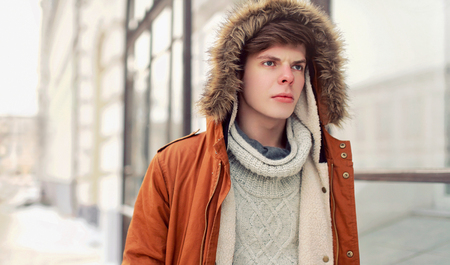 Fashion portrait young man walking in city wearing brown jacket with hood, knitted sweaterの写真素材