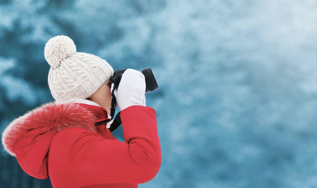 Woman in winter, female photographer takes picture on digital camera outdoors in cold day on blurred forest background, empty copy space, view profileの写真素材