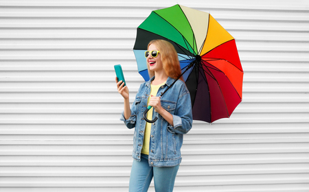 Happy woman laughing with smartphone having video call, holds colorful umbrella on white backgroundの写真素材