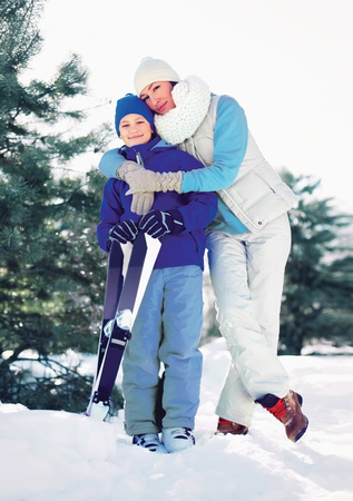Mother hugging child with ski in winter forestの写真素材