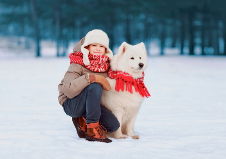Portrait of smiling child walking with white Samoyed dog in winter day at parkの写真素材