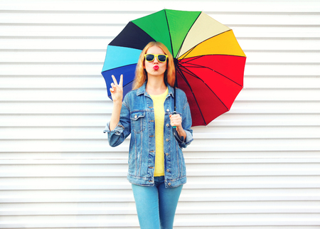 Fashion cool girl with colorful umbrella makes an air kiss on white background in cityの写真素材