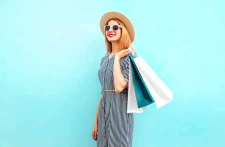 Fashion portrait woman walks with shopping bags in striped dress, summer round straw hat on blue backgroundの写真素材