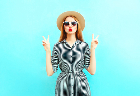 Fashion woman with red lips sends an air kiss in summer round straw hat on blue backgroundの写真素材