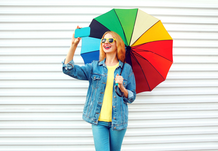 smiling woman takes picture self portrait on smartphone with colorful umbrellaの写真素材