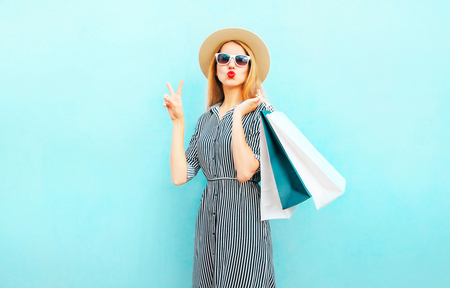 Fashion portrait pretty woman with shopping bags in striped dress, summer round straw hat on blue backgroundの写真素材