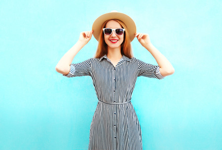 Fashion smiling woman wearing a striped dress, summer straw hat on blue backgroundの写真素材