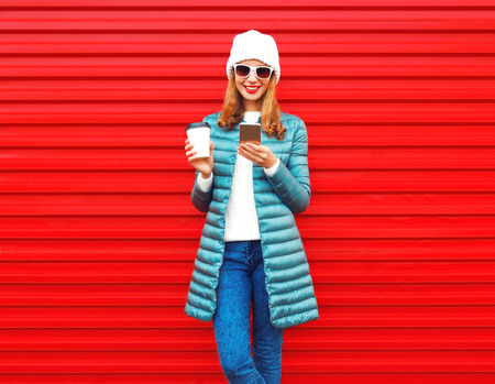 Fashion young woman is using smartphone with coffee cup on a red background in the cityの写真素材