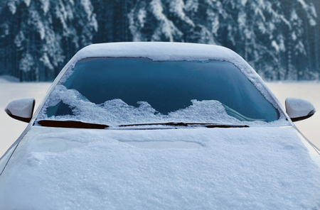 Frozen winter car covered snow, view front window windshield and hood on snowy forest backgroundの写真素材
