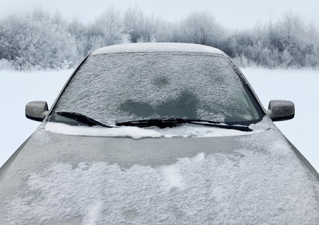 Frozen winter car covered snow, view front window windshield and hood on snowy forest backgroundの写真素材