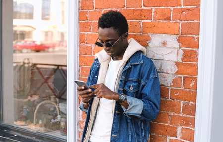 portrait cool urban african man with phone on city street over brick wall backgroundの写真素材