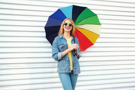Happy smiling young woman holding colorful umbrella in hands on white wall backgroundの写真素材