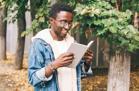 Portrait happy smiling african man reading book in autumn city parkの写真素材