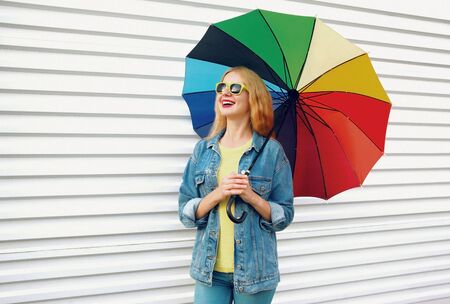 Portrait happy smiling woman holding colorful umbrella on white wall backgroundの写真素材