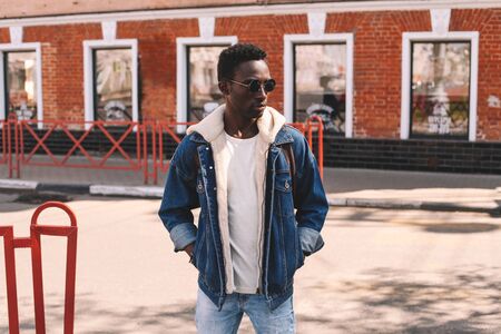 Stylish african man wearing jeans jacket standing on evening city streetの写真素材