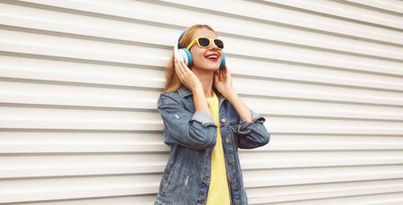 Cool girl in wireless headphones enjoying listening to music on city street over white wall backgroundの写真素材