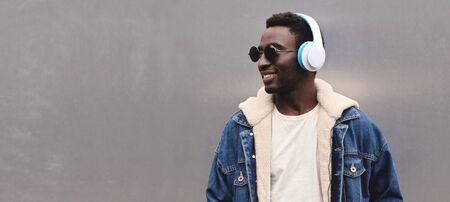 Portrait happy smiling african man in wireless headphones listening to music looking away at blank copy space gray metal wall backgroundの写真素材