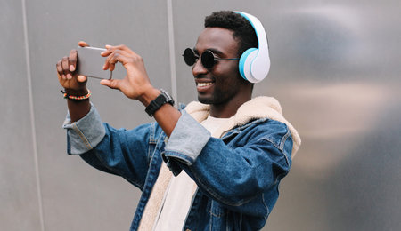 Modern happy smiling young african man taking selfie picture by smartphone while listening to music...