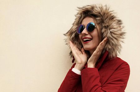 Portrait close up happy smiling surprised young woman looking away with blank copy space wearing red jacket with fur hood over backgroundの写真素材
