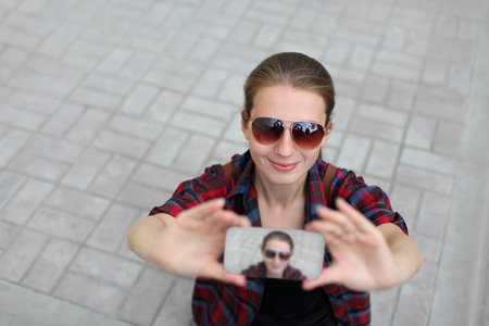 Young woman taking selfie picture by smartphone over city street background, top view