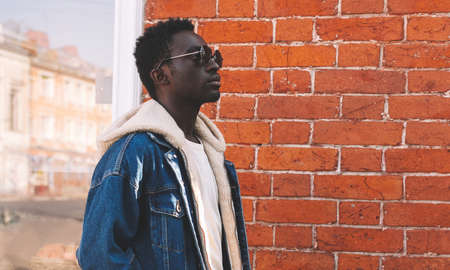 Portrait of stylish young african man model posing on a city street over brick wall backgroundの写真素材
