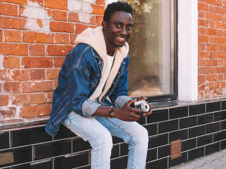 Portrait of happy smiling african man photographer with vintage film camera on city streetの写真素材
