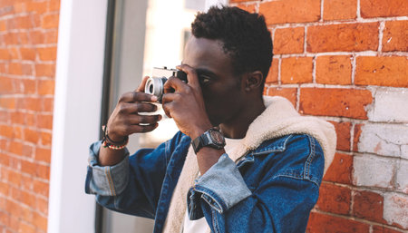 Portrait close up of african man photographer with vintage film camera taking picture while walking...