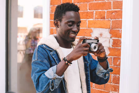 Portrait of happy smiling african man photographer with vintage film camera taking picture walking on city streetの写真素材