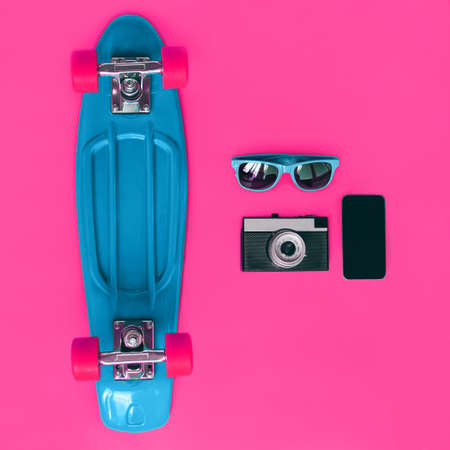 Colorful stylish set, blue skateboard, sunglasses, vintage film camera and smartphone screen on a pink background, top view, flat layの写真素材