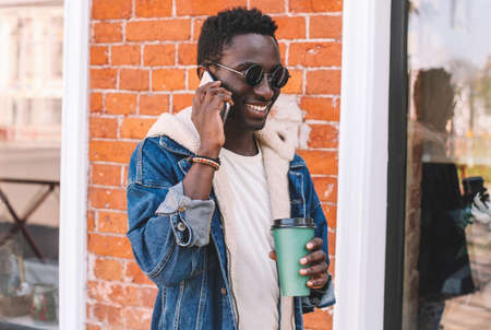 Portrait of happy smiling african man talking on smartphone on a city streetの写真素材
