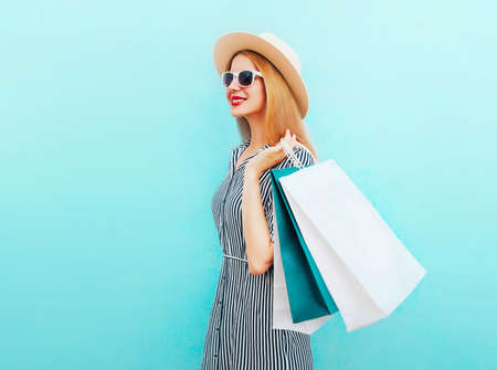 Happy smiling woman with shopping bags wearing a summer straw round hat, black white striped dress on a blue backgroundの写真素材